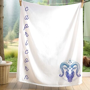 May include: White throw blanket with the word "Capricorn" spelled vertically down the left side and a blue and purple illustration of a goat's head with horns in a circle.
