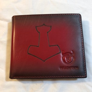 May include: A red leather wallet with a black gradient. The wallet has a embossed design of a hammer and a bull's head with the text "BULLCAPTAIN".