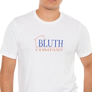 Peut inclure: T-shirt blanc avec l'inscription "BLUTH COMPANY" en bleu et orange. Le design comprend un contour de maison au-dessus du nom de l'entreprise. Le t-shirt est un col rond et semble être fait d'une matière douce.