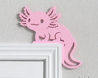 May include: A light pink axolotl wall decoration designed to sit on the corner of a door frame. The cutout features the stylized shape of an axolotl with its signature feathery external gills, a curved tail, and a simple, friendly facial expression.
