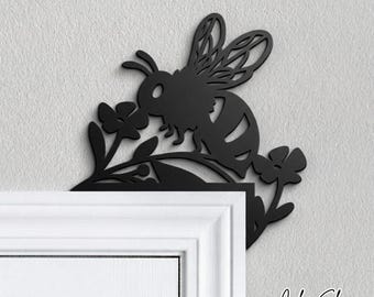 May include: Black metal bee and flower wall decor. The bee is perched on a floral branch, designed to be placed on a corner. The color shown is black.