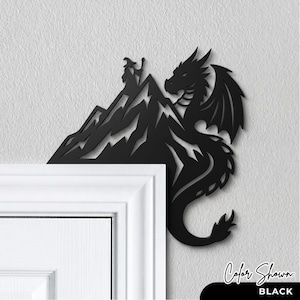 May include: A black metal door corner accent featuring a silhouette of a dragon perched on a mountain peak with a wizard figure standing at the summit. The design is flat and cut out, intended to be mounted on the corner of a door frame.