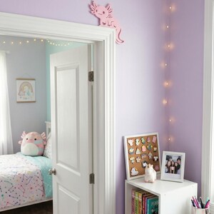 Peut inclure: Int&eacute;rieur de chambre lilas avec une porte blanche et une d&eacute;coration axolotl rose. Une &eacute;tag&egrave;re blanche pr&eacute;sente des livres, une photo encadr&eacute;e et un tableau en li&egrave;ge avec des &eacute;pingles. Le texte "LUCKYBORDERS.ETSY.COM" est visible en bas.