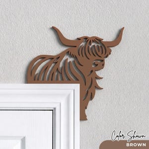 Pu&ograve; includere: Una decorazione da parete piatta, tagliata al laser e di colore marrone, a forma di testa e spalle di una mucca Highland. Il design presenta linee fluide e stilizzate che rappresentano il pelo folto e le lunghe corna ricurve dell'animale.
