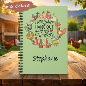 May include: A spiral-bound notebook with a light green cover. The cover features a wreath of cartoon chickens and the text "I just want to hang out with my chickens" and the name "Stephanie".