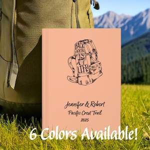 May include: A peach-colored journal with a black illustration of a backpack and the text "Backpacking is Life." The journal also includes the names "Jennifer & Robert," "Pacific Crest Trail 2025," and "6 Colors Available!" A green backpack is in the background.