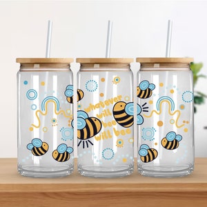 Può includere: Tre bicchieri di vetro trasparente con coperchi in bambù e cannucce. Ogni bicchiere presenta un diverso design di api con il testo "whatever will bee will bee".