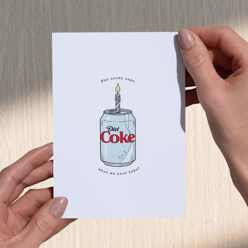 May include: A greeting card featuring a Diet Coke can with a lit birthday candle on top. The can is light blue with the red 'Diet Coke' logo. The text above reads 'Who needs cake' and below 'when we have coke?' The card is held by two hands.