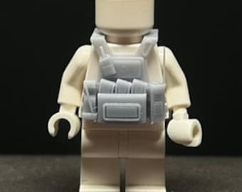 May include: A white Lego minifigure wearing a gray tactical vest with pouches. The vest has a large rectangular pouch in the center.