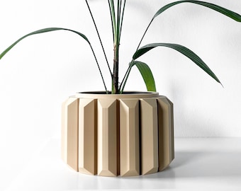 Könnte beinhalten: Eine grüne Zimmerpflanze mit langen, schmalen Blättern in einem beigefarbenen, geometrischen Topf. Der Topf hat ein geripptes Design und eine abgerundete Form.