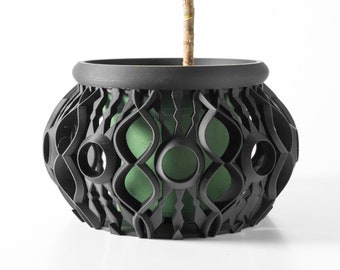 May include: A black planter with a geometric design and a green plant inside. The planter has a round shape and is made of a sturdy material.