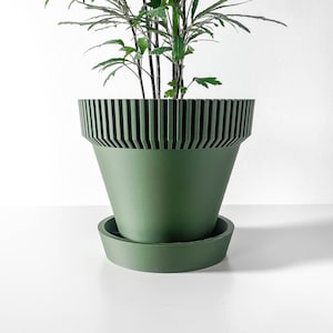 May include: A green planter with a ribbed design and a matching saucer. The planter is empty and ready to be filled with a plant.