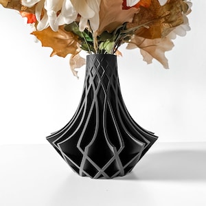 May include: A black geometric vase with a lattice design holds a bouquet of dried flowers with white, orange, and brown petals.