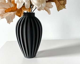May include: A black vase with vertical lines, holding dried flowers with white petals and brown leaves.