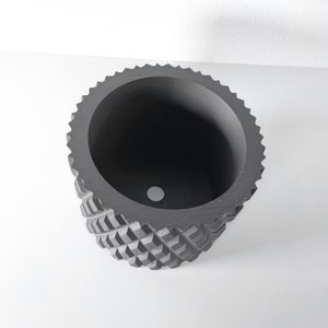 May include: A black geometric planter with a textured, diamond-shaped pattern. The planter has a round opening at the top and a drainage hole at the bottom.