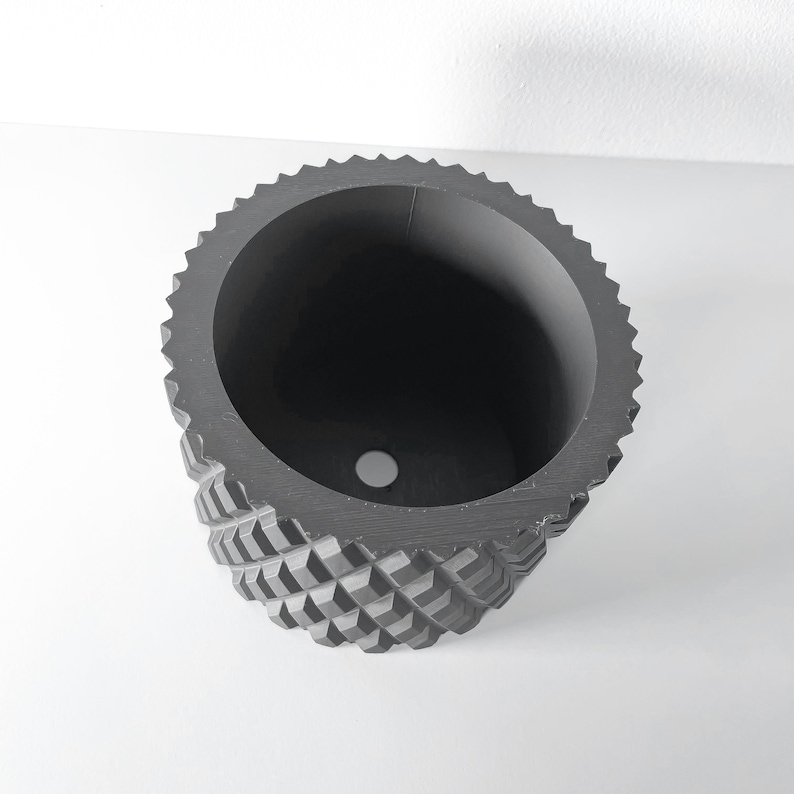May include: A black geometric planter with a textured, diamond-shaped pattern. The planter has a round opening at the top and a drainage hole at the bottom.