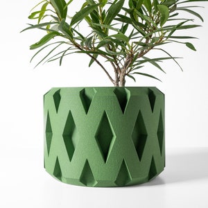 May include: A green planter with a diamond pattern design. The planter is made of a textured material and has a round shape. A green plant is growing inside the planter.
