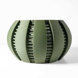 May include: A green, round planter with a geometric design. The planter has a series of vertical and horizontal lines that create a grid pattern.