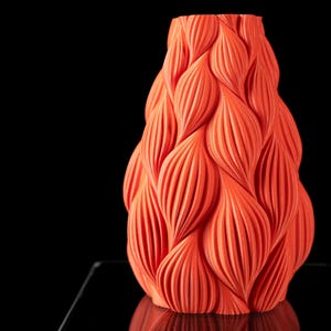 May include: A bright orange ceramic vase with a unique, textured, wavy design. The vase is shaped like a teardrop and has a smooth, glossy finish.