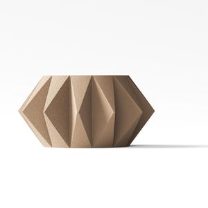 May include: A beige, cylindrical container featuring a textured, geometric exterior with repeating triangular facets. The object has a wide, open top and a flat base, showcasing a structured, angular design with a matte finish throughout the surface.
