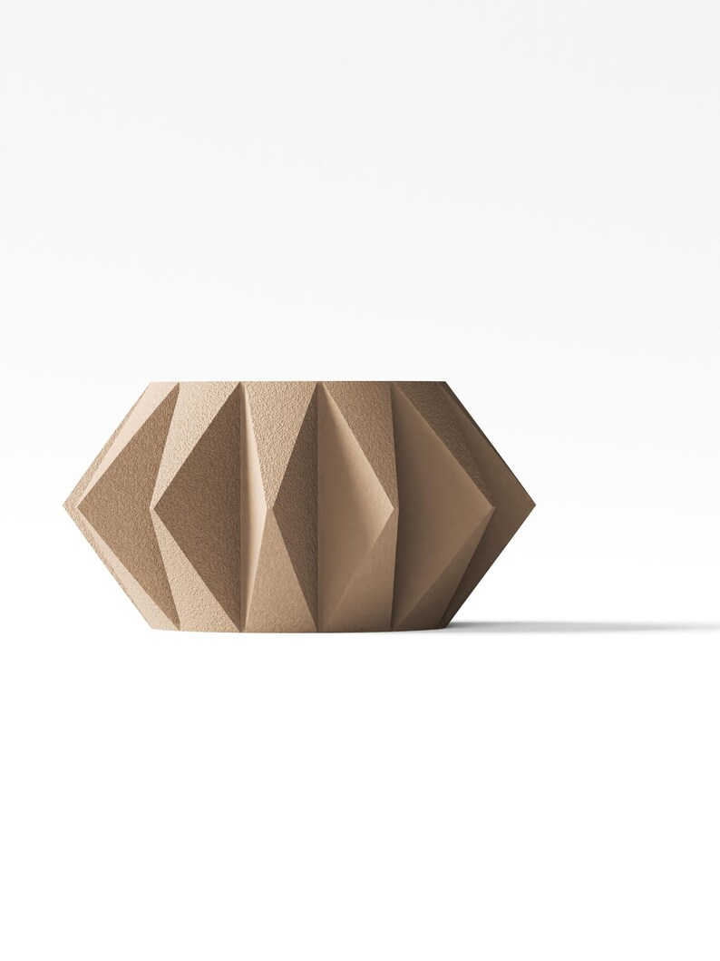 May include: A beige, cylindrical container featuring a textured, geometric exterior with repeating triangular facets. The object has a wide, open top and a flat base, showcasing a structured, angular design with a matte finish throughout the surface.