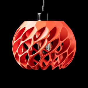May include: A red, 3D printed pendant light fixture with a geometric, honeycomb-like design. The light fixture is hanging from a black cord and has a visible light bulb inside.