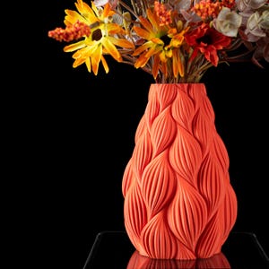 May include: A bright orange vase with a textured, wavy design. The vase is filled with a bouquet of yellow and orange flowers.