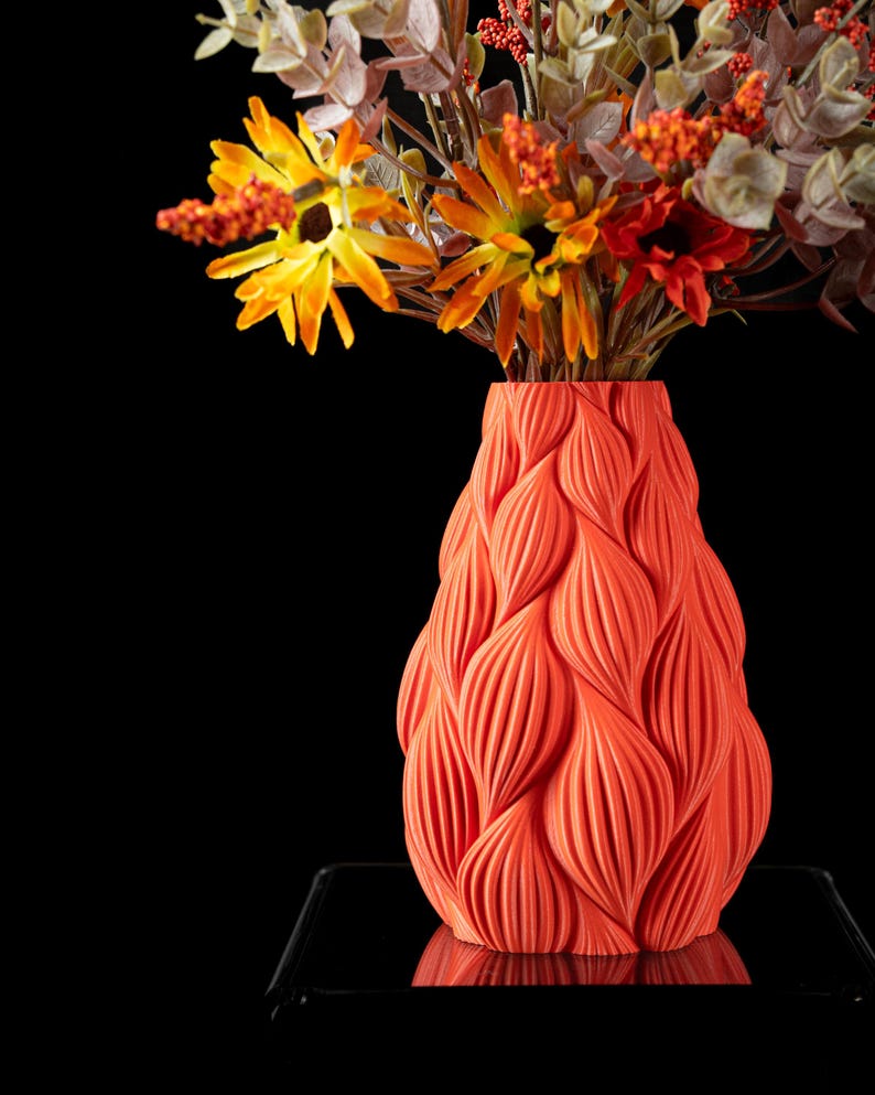 May include: A bright orange vase with a textured, wavy design. The vase is filled with a bouquet of yellow and orange flowers.