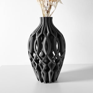 Può includere: Un vaso in ceramica nero con un design geometrico traforato. Il vaso è vuoto e ha una forma rotonda e bulbosa.