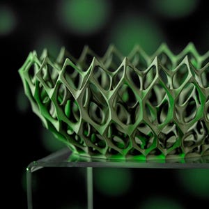 May include: A green, geometric, 3D printed bowl with a honeycomb pattern. The bowl is sitting on a clear glass pedestal.