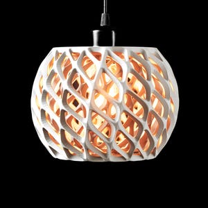 Könnte beinhalten: Weiße, kugelförmige Pendelleuchte mit einem geometrischen, durchbrochenen Design. Die Leuchte hängt an einem schwarzen Kabel vor einem schwarzen Hintergrund. Das Innere leuchtet warm, was einen auffälligen Kontrast erzeugt.