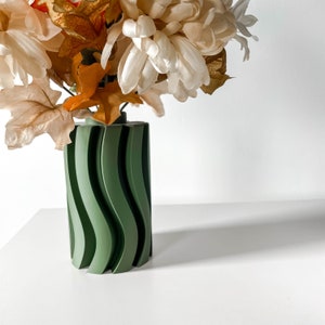 May include: A green ceramic vase with a wavy pattern, holding a bouquet of white and brown silk flowers.