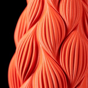 May include: Close-up of a bright orange 3D printed object with a textured, wavy pattern.