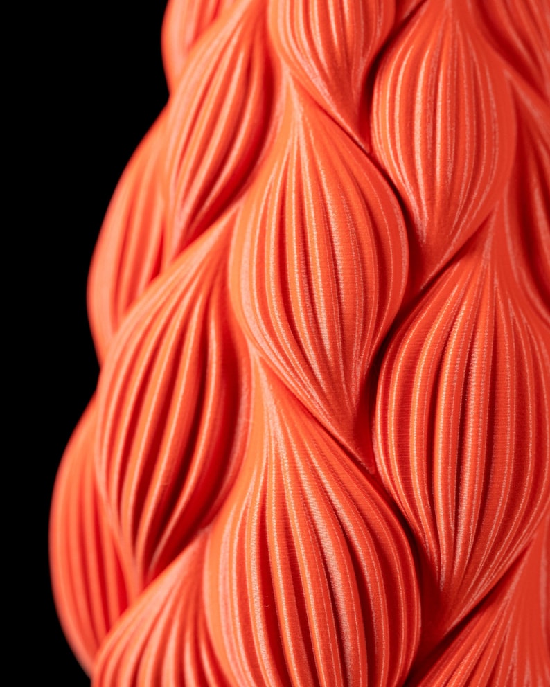 May include: Close-up of a bright orange 3D printed object with a textured, wavy pattern.