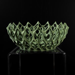 May include: A green, geometric bowl with a delicate, openwork design. The bowl is made of a lightweight material and has a unique, modern aesthetic.