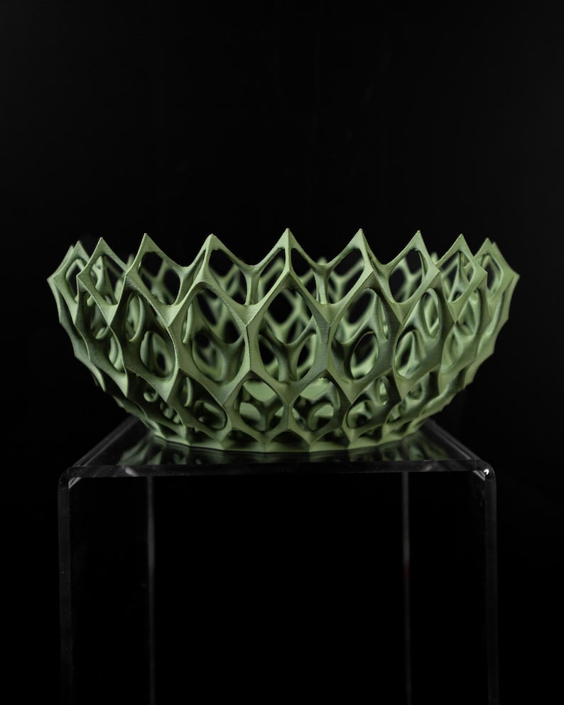 May include: A green, geometric bowl with a delicate, openwork design. The bowl is made of a lightweight material and has a unique, modern aesthetic.