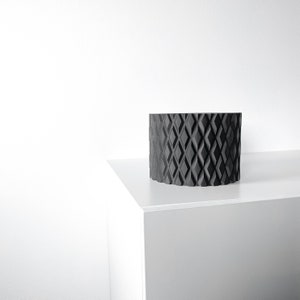 May include: A black geometric planter with a diamond pattern sits on a white surface.