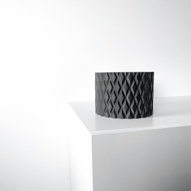 May include: A black geometric planter with a diamond pattern sits on a white surface.