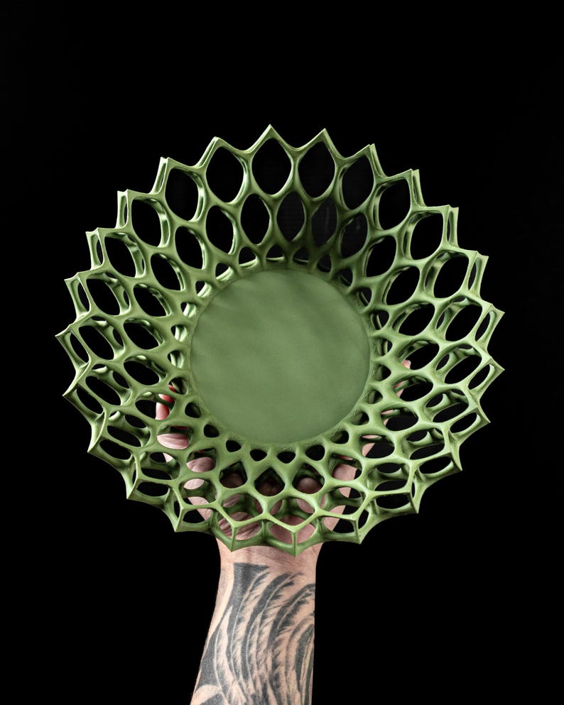 May include: A green ceramic bowl with a geometric, openwork design. The bowl is held in a hand with a tattoo.