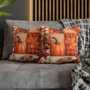 May include: Two square throw pillows featuring a patchwork design with orange pumpkins, autumn leaves, and berries. The pattern includes orange and white checkered squares, solid orange sections, and cream-colored borders with floral motifs.