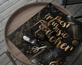 May include: A wrapped gift with a brown ribbon and a sheet of black wrapping paper with gold musical instrument illustrations and the text "Best Music Teacher". A roll of tape and scissors are also on the table.