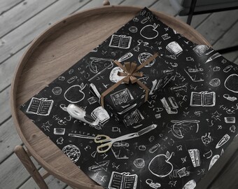 May include: A wrapped present with a brown ribbon on black wrapping paper featuring white school-themed doodles. The paper is on a wooden table with scissors and tape. The doodles include apples, books, and globes.
