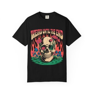 Op de afbeelding: Zwart t-shirt met een grafisch ontwerp van een schedel met bloemen, paddenstoelen en vlammen. De tekst "WEIRD UNTIL THE END" staat in een retro lettertype. Een uniek en opvallend ontwerp.