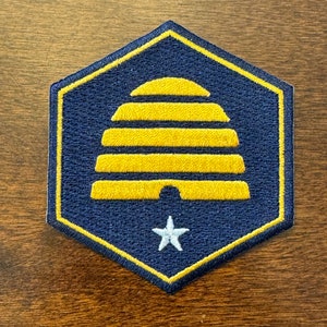 May include: A blue and gold hexagonal patch with a yellow beehive and a white star in the center.