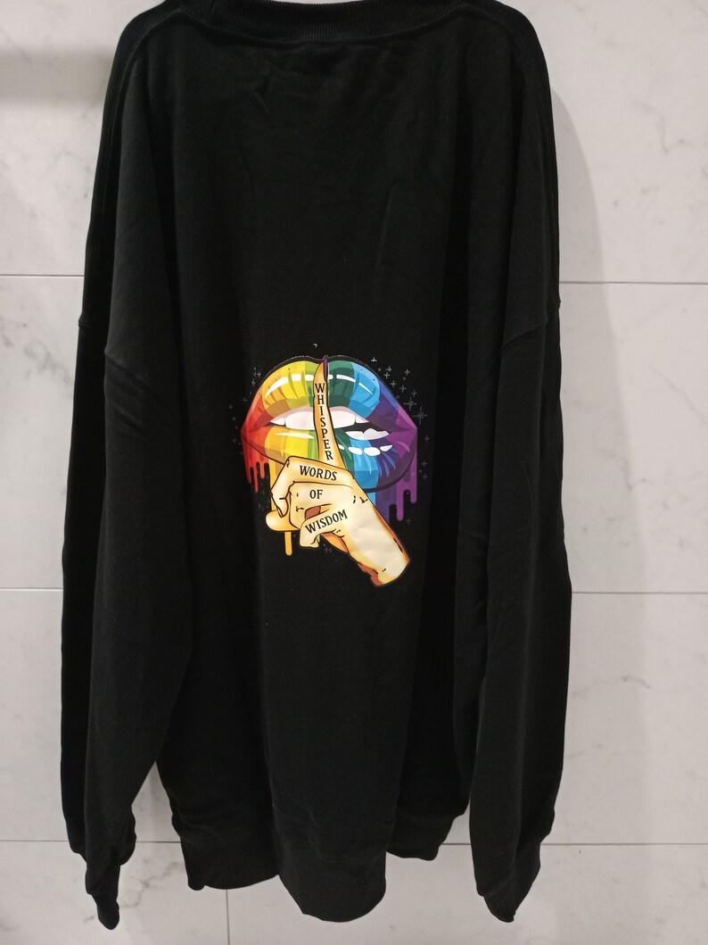 Pu&ograve; includere: Felpa nera con una grafica di labbra arcobaleno e il testo "Whisper Words of Wisdom".
