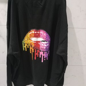 Pu&ograve; includere: Felpa nera con un design di labbra glitter arcobaleno sul retro.