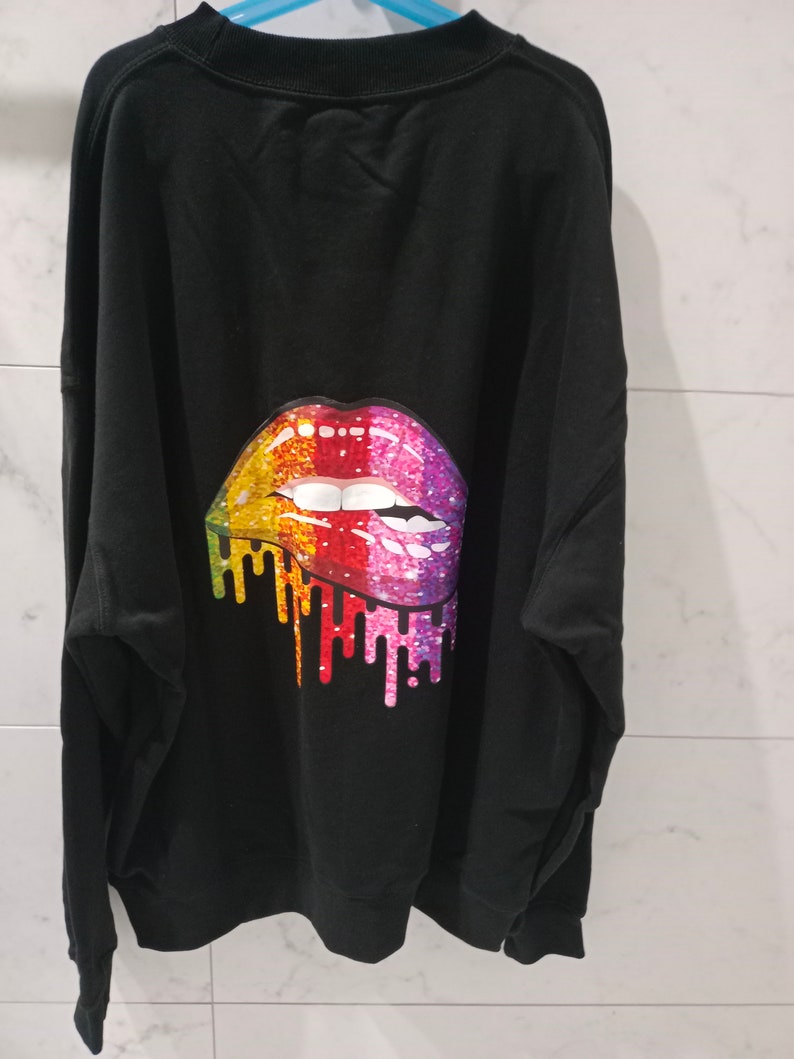 Pu&ograve; includere: Felpa nera con un design di labbra glitter arcobaleno sul retro.