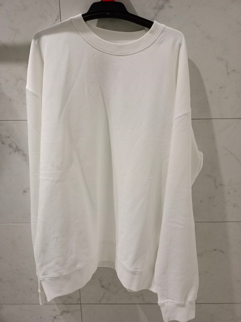 Pu&ograve; includere: Una felpa bianca a maniche lunghe con collo rotondo.