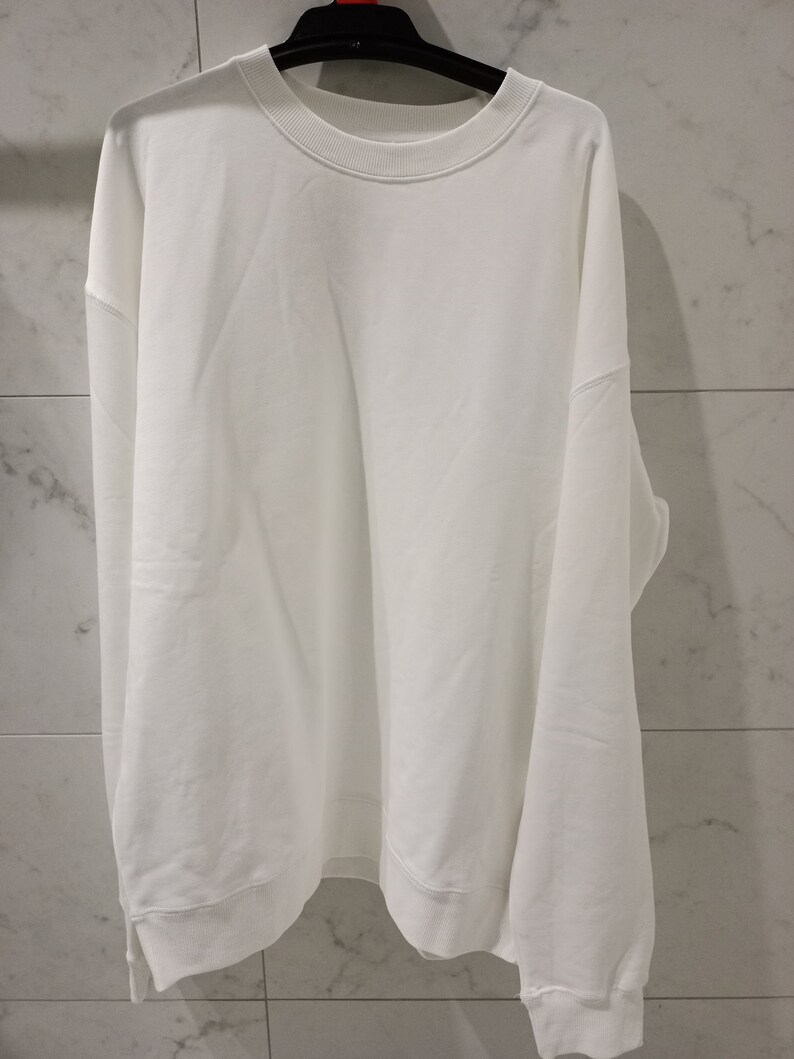 Pu&ograve; includere: Una felpa bianca a maniche lunghe con collo rotondo.