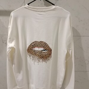 Pu&ograve; includere: Felpa bianca con un design di labbra a stampa leopardata sul retro.
